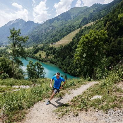 Ein Läufer läuft einen Berg hinauf, im hintergrund ein gletscherblauer Bergsee. 