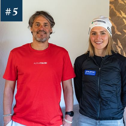Das Bild zeigt zwei Personen, die lächeln. Der Mann links trägt eine rotes T-Shirt, die Frau rechts trägt eine dunkelblaue Jacke mit Sponsorenlogos und eine weißen Mütze. <br/>Der Mann links heißt Stefan Steinacher und die Dame rechts Johanna Hiemer.