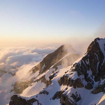 Ein Foto vom Gipfel zeigt wie ein anderer Berg von der Sonne angescheint wird.