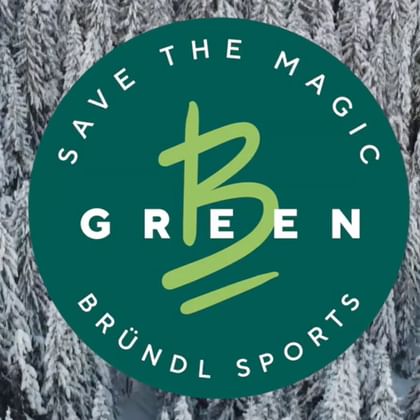 Zu sehen ist ein Wald voller verschneiter Bäume. In der Mitte ist das B-Green Logo von Bründl Sports zu sehen mit Save the Magic.