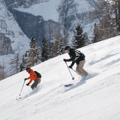 Two skiers descending through fresh powder snow in alpine terrain, wearing functional Martini ski touring apparel.