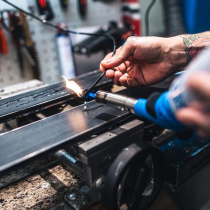 A Bründl Sports service technician repairs a ski base using a flame and filling material. The image captures precise craftsmanship in the ski service workshop.