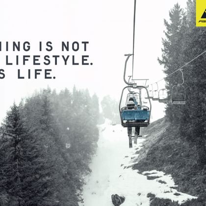 A skier sits alone on a chairlift in falling snow, surrounded by snowy trees – featuring the slogan “Skiing is not a lifestyle. It’s life.” and the Fischer logo.