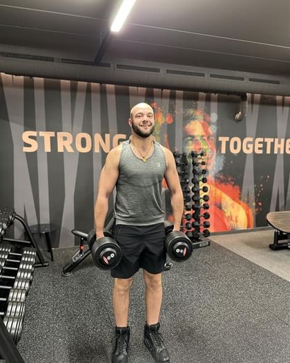 The picture shows a Bründl Sports employee in the gym holding dumbbells.