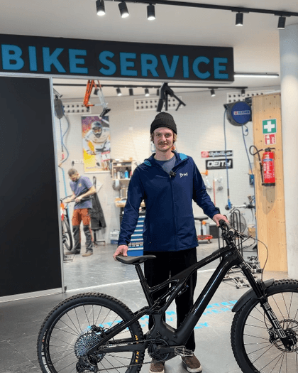 Bründl Sports employee stands with a mountain bike in front of the Bründl Sports bike workshop