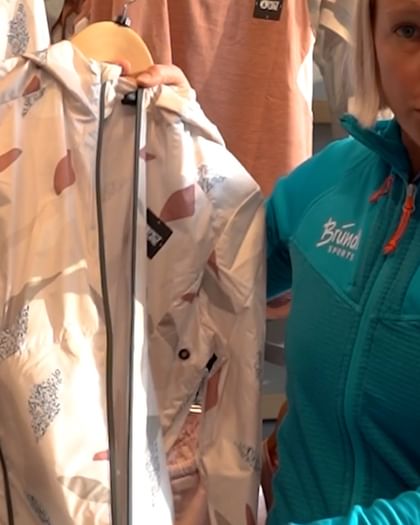 Bründl Sports employee stands in front of a wall and presents a sustainable jacket from Picture Clothing.