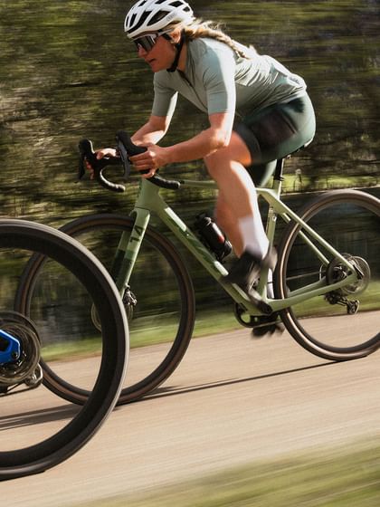 Female cyclist in green Löffler outfit riding fast on a road