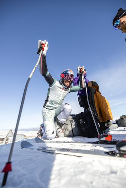 Marcel Hirscher kniet am Schnee und lacht mit seinem Team, während er Aufwärmübungen macht.