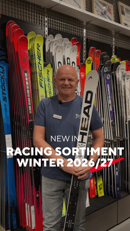 Bründl Sports Mitarbeiter steht mit einem HEAD Rennski vor einer großen Auswahl an Ski im Shop. Im Bild steht „New in Racing Sortiment Winter 2026/27“.