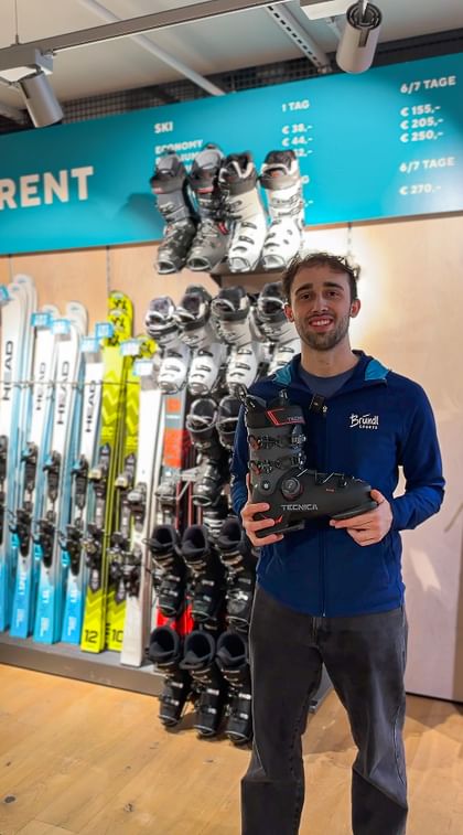 Ein Bründl Sports Mitarbeiter steht vor der Skiverleih Wand und hält einen Skischuh in der Hand. 