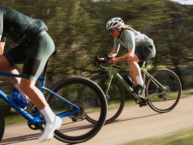 Two road cyclists in green Löffler apparel riding fast on a scenic road